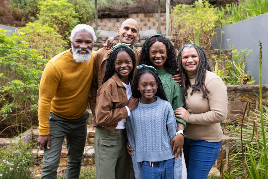 Diverse family standing on steps in garden under pergola wearing knit headbands smiling at viewer