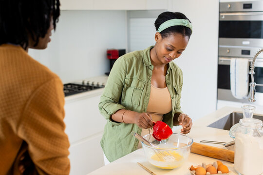 African American couple baking at kitchen island using red measuring cup over glass mixing bowl