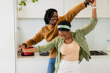 African American couple dancing together in modern home kitchen twirling near red toaster