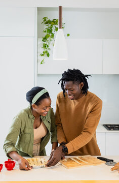 African American couple at kitchen island weaving dough lattice on boards with red bowls