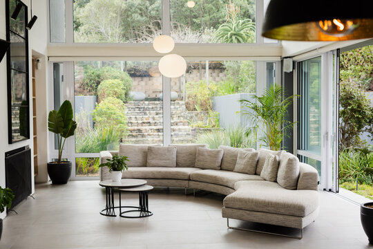 Light gray curved sofa is anchoring living room, coffee tables are facing windows and garden