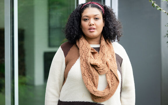 Woman standing and wearing brown sweater infinity scarf red headband at modern building entrance