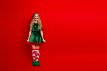 Festive woman dressed as a joyful Christmas elf posing with a playful smile against a vibrant...