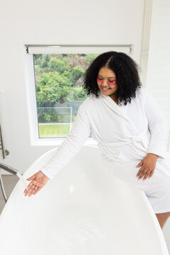 African American woman testing water from chrome faucet wearing gel patches in bathroom, copy space