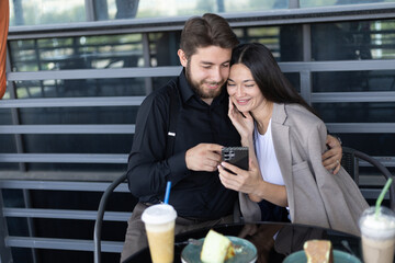 A couple is sitting at a table, looking at a smartphone together and smiling.