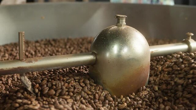 Close up roasted coffee beans mixing in mixer roaster blend automatic metal drum machine stirring roasting cocoa caffeine at production facility aromatic grains in grinder industrial food preparation