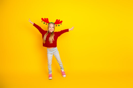 Playful Christmas joy young girl in red sweater with reindeer headband leaps on bright yellow backdrop for festive holiday celebration - Powered by Adobe