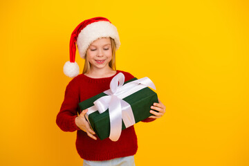 Funny festive gift moment as a cheerful young girl in a Santa hat presents a green wrapped box against a bright yellow backdrop