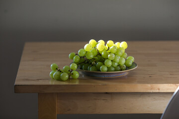Fresh green grapes on a plate illuminated by backlight, highlighting texture and freshness