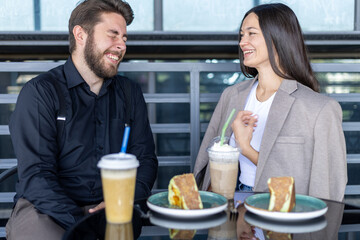A couple are smiling and talking to each other while having drinks and cake.