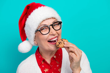 Woman in santa hat enjoys a cookie in a festive scene with teal background celebrating christmas...