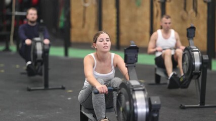 Emotional sporty young girl doing functional strength training, working out on rowing machine in modern gym - Powered by Adobe