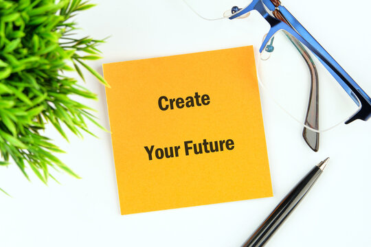 A bright yellow sticky note placed on a clean surface features the phrase Create Your Future. Accompanying the note are stylish glasses and a sleek pen, promoting a positive mindset