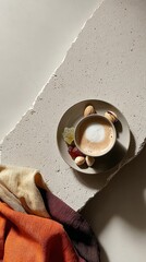 Cappuccino in gray cup with nuts and candy on light stone surface and colorful fabrics