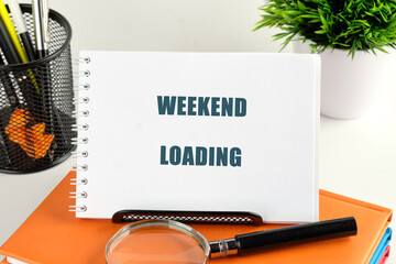 A sign reading weekend loading rests on an organized desk surrounded by stationery and a small green plant, evoking excitement for the approaching break and relaxation