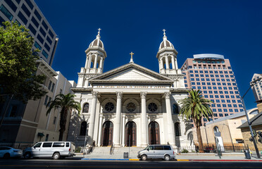 Obraz premium Front view of the Cathedral Basilica of St. Joseph in downtown San Jose, California, United States showcasing its neoclassical facade with twin bell towers and Corinthian columns under a vivid blue