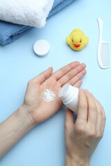 Woman with bottle of talcum powder and baby accessories on light blue background, flat lay