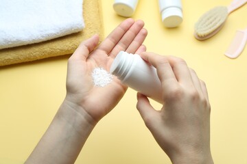 Woman with bottle of talcum powder and baby accessories on yellow background, top view