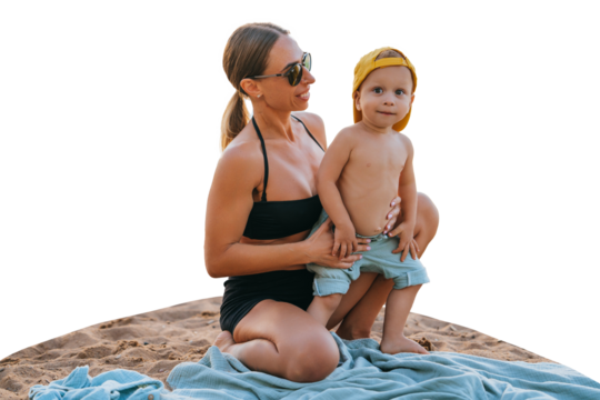 Healthy caucasian boy spending time with mom sits on plaid  against transparent background. Pretty woman in black swimsuit hugging son at seashore wears sunglasses
