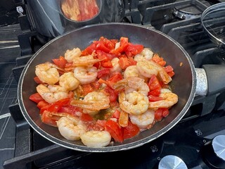Cooking shrimps with tomatoes in frying pan on stove at home, closeup