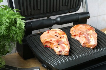 Electric grill with uncooked steaks and herbs on wooden table, closeup