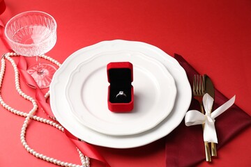Beautiful table setting for romantic dinner and box with engagement ring on red background