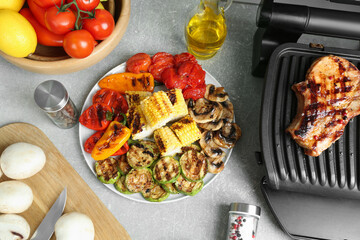 Electric grill with steak and grilled vegetables on light table, flat lay