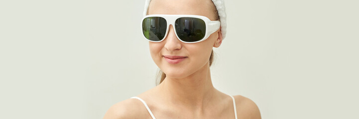Fototapeta premium Caucasian young female smiling wearing large white sunglasses with neutral background.