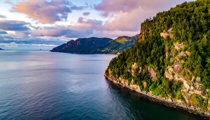 An aerial view showcases a rugged coastline merging with the ocean. The sky is painted with soft colors as the sun begins to set over the landscape