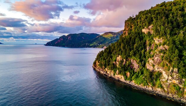 An aerial view showcases a rugged coastline merging with the ocean. The sky is painted with soft colors as the sun begins to set over the landscape