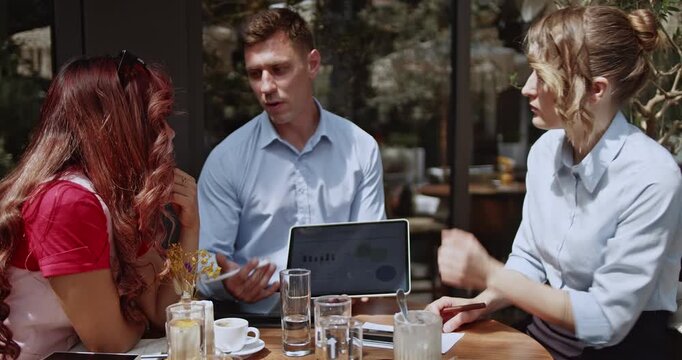 Business partners engage in a productive outdoor meeting, analyzing charts and discussing strategies on tablet. This dynamic collaboration showcases teamwork and innovation in a modern, relaxed cafe.
