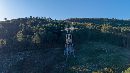 Electricity pylon standing on green hill distributing power