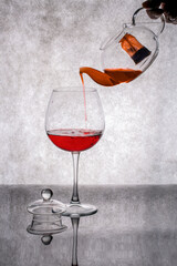 Pouring wine from a teapot into a glass on a gray background