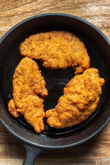 Southern fried chicken cooked in a cast iron frying pan with cooking oil. On a wooden board background..