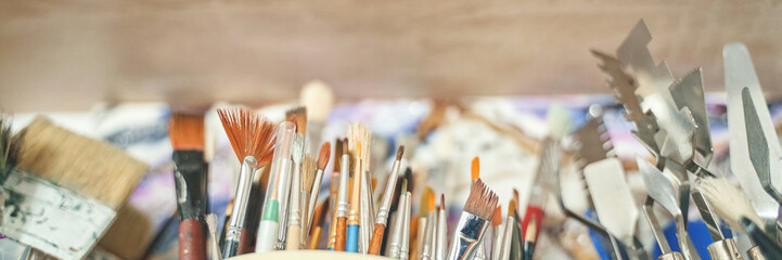 Fototapeta premium Assortment of various art tools including brushes and palette knives in creative workshop.