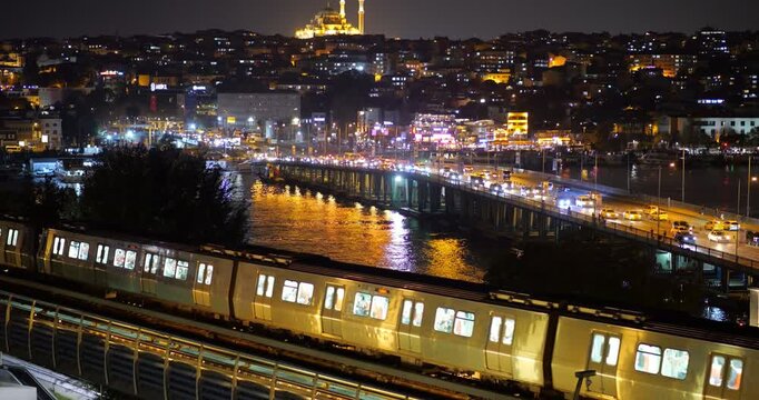 Metro train approach Golden Horn bridge station at night, moderate car traffic on Ataturk Bridge, and dark Fatih cityscape on background. Characteristic slow motion view of Istanbul city at night