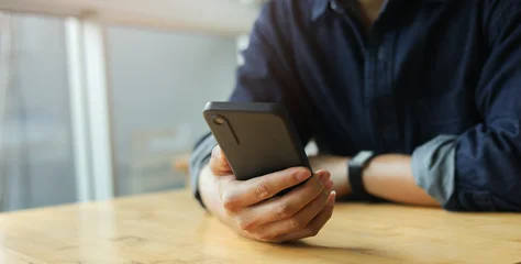 Fototapete Wohnzimmer close up businessman hand hold smartphone to surfing the internet and check work or mail on website while sit in the living room in weekend for business technology and lifestyle concept  © chinnarach