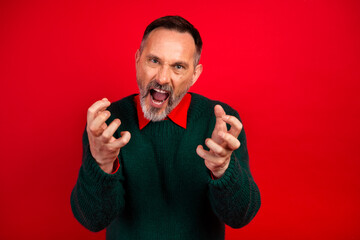 Funny mature man in green sweater shouting with wide hands against red background for holiday Christmas mood and shop promo featuring Christmas cheer and festive energy