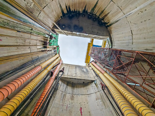 Looking up from the bottom of a deep drainage tunnel shaft showing concrete walls, ventilation...