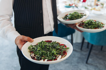 Waiter in uniform serving dishes and drinks on party, server carrying plates with food and...