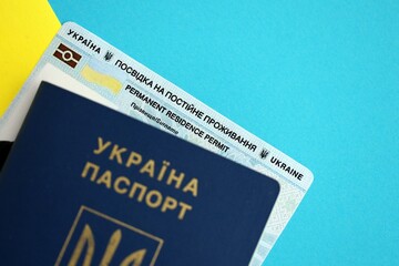 Ukrainian residence permit card or permanent resident card with passport on Ukraine flag close up