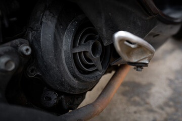Macro view of a motorcycle engine and exhaust section, showing the vent cover, bolts, and rusty pipe with dirt and wear marks, emphasizing mechanical texture and aging details.