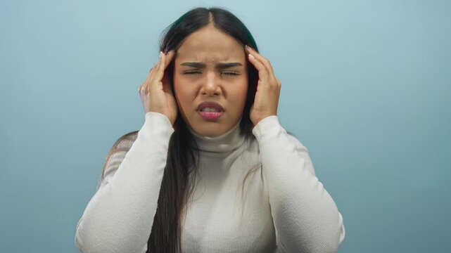 Young woman experiencing headache with hands on temples against a soft blue background, expressing discomfort and tension.