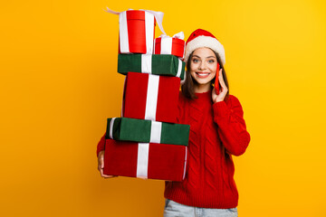 Funny Christmas shopper woman talking on phone with tall stack of gifts smiling in bright yellow...