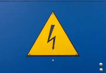 A bright yellow triangular warning sign with a black lightning bolt