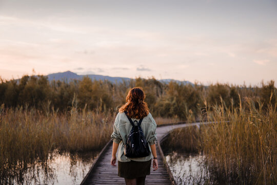 Adventurous hiker girl walking on wooden bridge over mountain lake