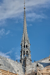 The Gothic spire of Notre Dame in Paris rising above the cathedral's transept with a blue sky and architectural details