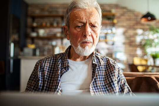 Senior man using laptop at home - Powered by Adobe