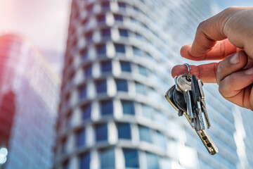 Hand Holding Keys Against Glass Office Towers – Concept of Property Ownership and Corporate Access