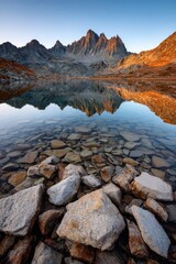 Majestic mountain peaks reflect in a clear lake surrounded by rocky terrain at sunrise